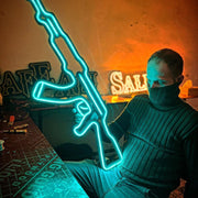 a man holding a teal colored AK-47 Neon Sign with black acrylic backing | ManhattanNeons